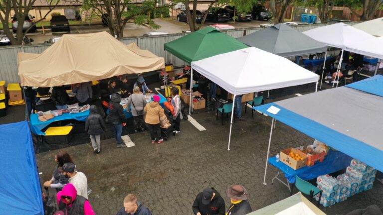 Outdoor charity drive under tents in a parking lot with volunteers sorting and distributing donated goods.