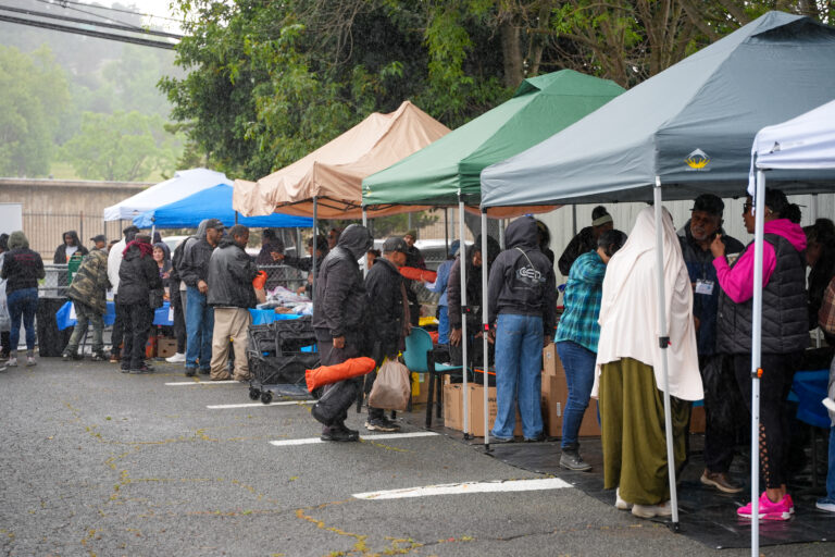 People under canopy tents in a rainy parking lot, sorting and distributing donated goods at a community relief event.